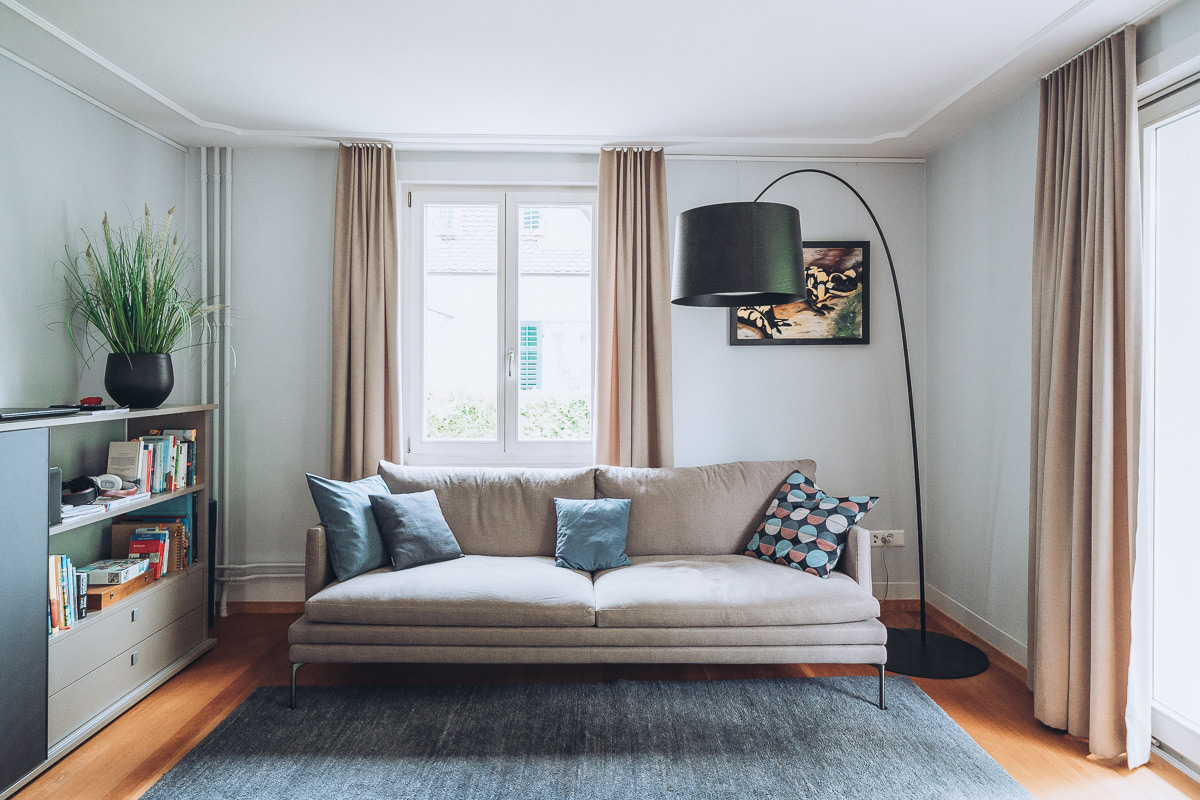 Ansicht einer Wohnungseinrichtung mit Holzm&ouml;beln, gepolstertem Sofa und Vorh&auml;ngen
